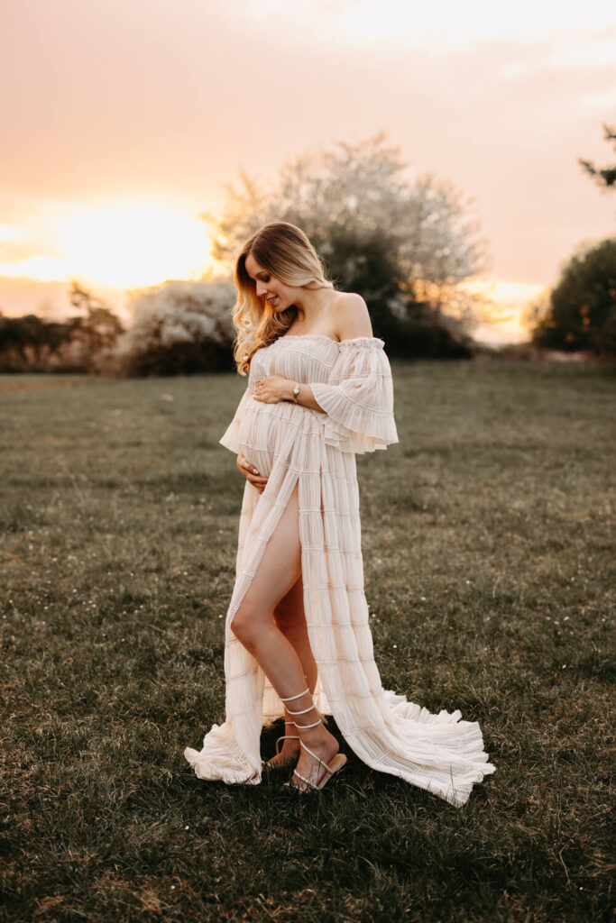 Schwangere Frau steht auf einer Wiese und hält ihren Babybauch beim Babybauch Shooting in Alsfeld Wenn ihr die besondere Zeit eurer Schwangerschaft mit einem Babybauch Shooting fotografisch von mir festgehalten haben möchtet, dann meldet euch frühzeitig bei mir, um euren Wunschtermin zwischen der 30. und 36. SSW zu sichern. Das Babybauch Shooting kann gerne draußen in der freien Natur stattfinden oder in meinem Studio. Für das Babybauch Outdoor Fotoshooting in der freien Natur, können wir auch einen zeitlichen Spielraum einplanen, falls das Wetter nicht mitspielt.